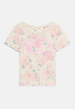 Κρεμ μπλουζάκι για μικρά παιδιά με ροζ λουλουδάτο σχέδιο και μεγάλο ροζ περίγραμμα κειμένου "GAP" στο εμπρόσθιο μέρος, κοντά μανίκια και στρογγυλή λαιμόκοψη.