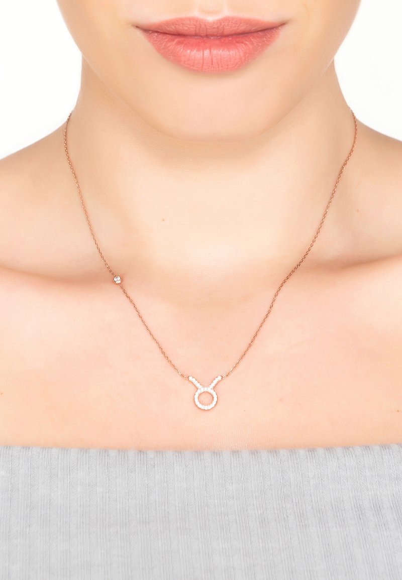 Rose gold necklace featuring a Taurus zodiac symbol accented with clear stones, resting on a smooth neck against a gray top.