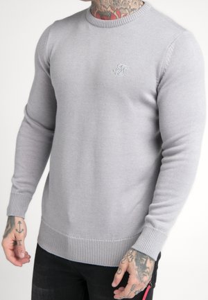 Pull en tricot gris clair avec un col rond, des poignets et un ourlet côtelés. Présente un petit logo brodé sur la poitrine.