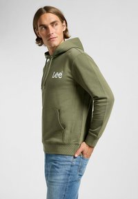 Felpa verde oliva con tasca frontale a forma di canguro e logo "Lee" ricamato in bianco. Presenta un cappuccio con coulisse e polsini a costine.