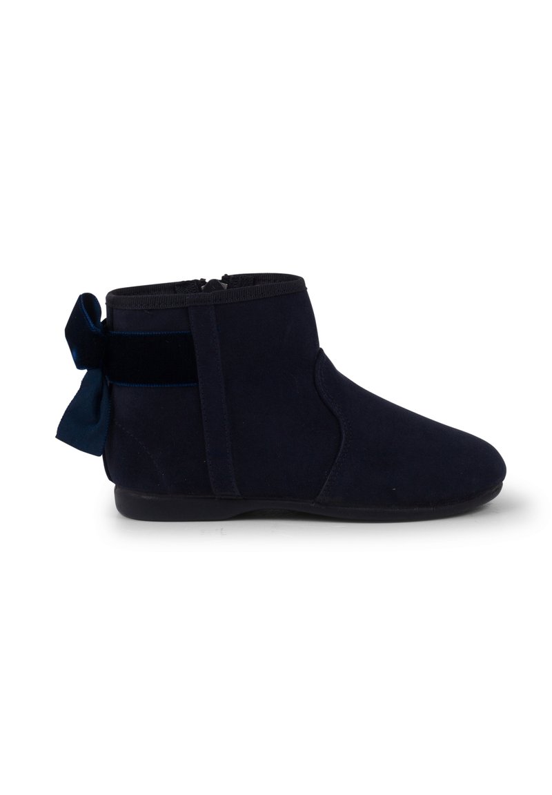 Stivaletti alla caviglia in suede blu navy con chiusura a cerniera laterale e un accento di fiocco in velluto sul tallone. Texture morbida e design con punta arrotondata.