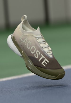 Zapatilla deportiva Lacoste con un diseño degradado en beige y marrón, parte superior de malla, cordones blancos y una suela texturizada con marca visible.