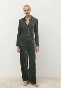 Conjunto de pijama de terciopelo en verde oscuro. Presenta una camisa de botón con cuello y mangas largas, combinada con pantalones de pierna ancha. Textura suave.