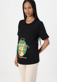 Black short-sleeve T-shirt featuring a graphic of a cartoon deer with a gift, surrounded by "Have a jolly Christmas" in playful lettering.
