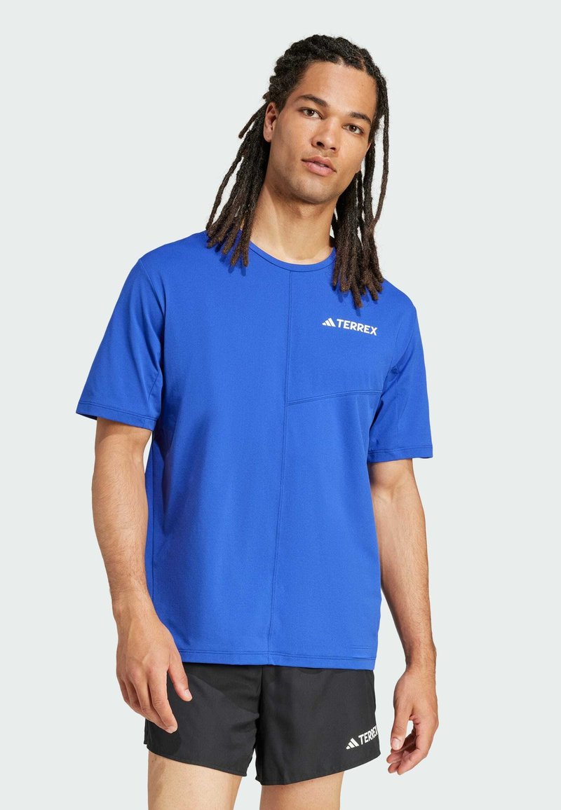 Blå kortärmad t-shirt i fukttransporterande tyg, med en framficka och en vit "TERREX"-logotyp på bröstet.