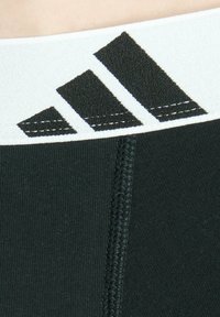 Fascia elastica nera per attività sportive realizzata in tessuto elastico, con cuciture bianche e un logo nero stampato con tre strisce diagonali.