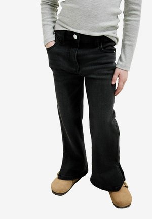 Svarta denimjeans med utställd design, utrustade med sidofickor och knäppning fram, tillsammans med beige slip-on skor.
