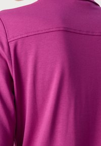 Aangesloten paarse kleding met een gladde textuur en zichtbare stiksels op de schouder. Geen patronen of extra details zichtbaar.