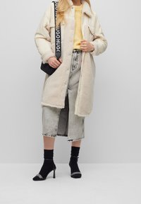 Gräddfärgad rock med fuskpälsfoder, gul stickad tröja, grå jeanskjol, svarta ankelsockor och svarta sandaler med silverdetalj.