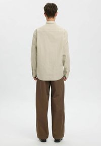 Heledatruud halli beežis ja oliivis, klassikalise krae ja pikkade varrukatega, kombineeritud lahtiste pruuni värvi pükstega.