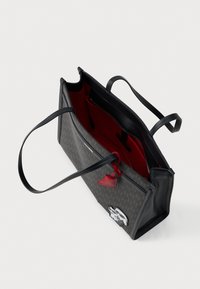 Torebka typu tote w ciemnobrązowym wzorze, z czarnymi uchwytami, czerwoną podszewką i srebrnym dekoracyjnym logo z przodu.