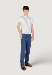 T-shirt bianco a girocollo, chinos blu e scarpe da barca marroni. La t-shirt presenta un piccolo logo, i chinos sono a taglio dritto con tasche.