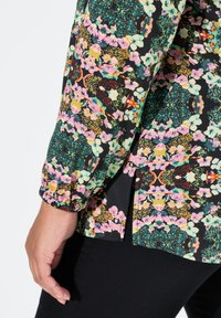 Blus med blommönster på svart bakgrund, med livfulla färger som rosa och grön. Mjuk tyg med detaljerad puffärm.
