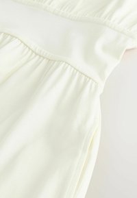 Helles cremefarbenes Kleid mit einem taillierten Oberteil, einem breiten, glatten Taillenbund und einem gerafften Rock. Weicher, dehnbarer Stoff mit subtiler Textur.