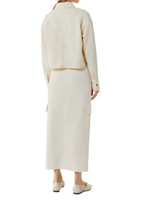 Kremowy dwuczęściowy zestaw składający się z krótkiej kurtki z długimi rękawami i spódnicy z wysokim stanem z bocznymi kieszeniami. Gładka tekstura materiału.
