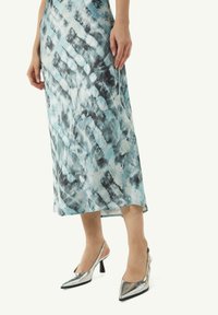 Maxikleid mit einem blau-schwarzen Batikmuster, aus leichtem Material gefertigt. Kombiniert mit silbernen, spitzen Heels und einem Slingback-Design.