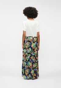 Haut blanc à manches courtes associé à une longue jupe fleurie arborant des motifs tropicaux colorés sur un fond noir.