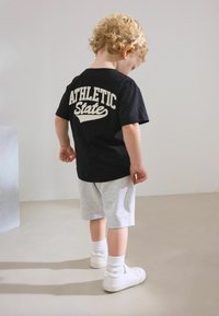 Svart bomull T-shirt med "ATHLETIC STATE" tryckt i vitt, kombinerad med grå sweatshorts. Vita sneakers och strumpor i ankellängd kompletterar outfiten.