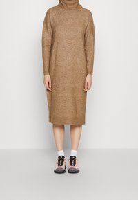 Robe en maille marron avec un col montant et des manches longues, associée à des baskets roses et noires. Texture lisse, design mi-long.