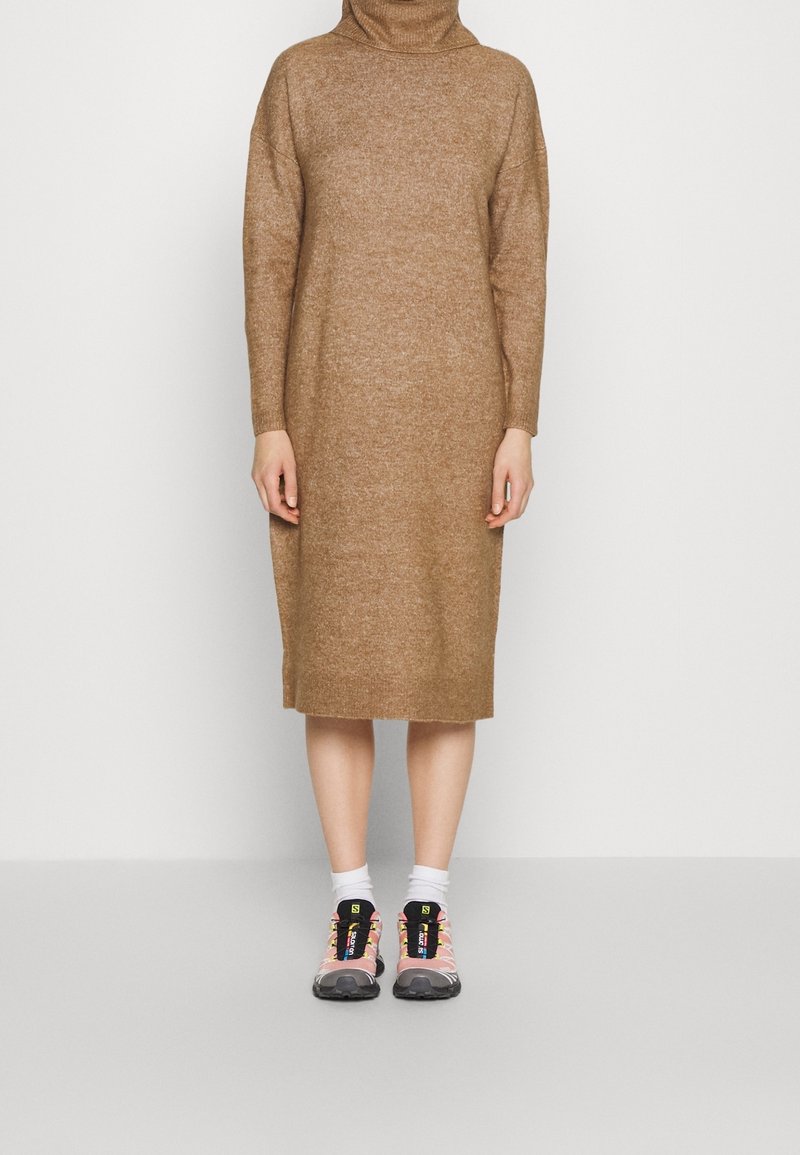 Robe en maille marron avec un col montant et des manches longues, associée à des baskets roses et noires. Texture lisse, design mi-long.