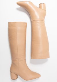 Knee-high beige leather boots with a pointed toe and a chunky heel, featuring a smooth texture and a fitted design.