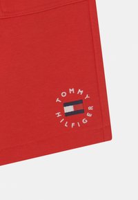 Calções de algodão vermelhos com um logótipo bordado branco em forma circular com "TOMMY HILFIGER" e um design de bandeira no centro. Textura suave, corte casual.