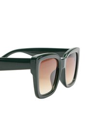 Zielone plastikowe okulary przeciwsłoneczne z dużymi kwadratowymi oprawkami, stopniowanymi brązowymi soczewkami i gładką fakturą. Posiadają szerokie zauszniki dla dodatkowej stabilności.