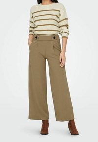 Pull rayé crème et marron à coupe ample, associé à un pantalon olive taille haute à jambes larges, avec deux poches avant et des détails à boutons.