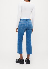 Modré džíny s rovnými nohavicemi a neopracovaným lemem, v kombinaci s bílým přiléhavým topem s dlouhým rukávem a černými platformovými botami.