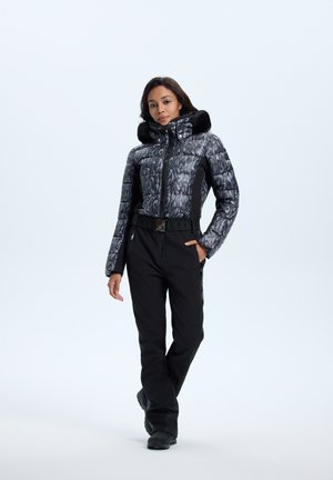 Padded jacket in black with metallic grey abstract pattern and faux fur collar; paired with black pants and black footwear.