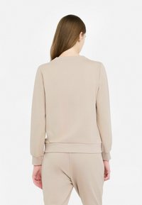 Felpa beige con maniche lunghe, collo rotondo e polsini elasticizzati. Tessuto liscio; abbinata a pantaloni beige coordinati.