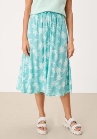 Une jupe mi-longue turquoise avec une taille à cordon, ornée de motifs de feuilles de palmier blanches. Confectionnée en tissu léger avec une silhouette fluide.