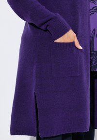 Lång lila cardigans i mjukt, strukturerat tyg, med slits på sidan och framficka, samt ribbade ärmslut och nederkant.