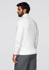 Biały sweter z golfem wykonany z miękkiego materiału, z długimi rękawami i dopasowanym krojem. W połączeniu z szarymi spodniami, widok z tyłu.