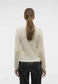 Maglione di lana a coste con lavorazione a maglia aperta. Maniche lunghe, design aderente e orlo arrotondato. Abbinato a pantaloni neri.