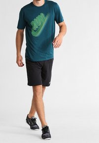 Teal kortärmad skjorta med en grön Nike-logotyp, parat med svarta shorts och svarta löparskor med vita detaljer.