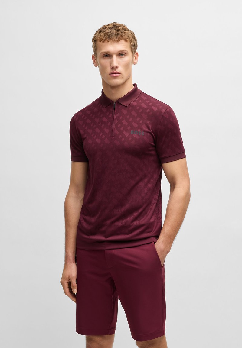 Bordeaux poloshirt med en subtil mønstret tekstur, korte ærmer og lynlås fortil. Parret med matchende shorts, begge i en ensfarvet farve.