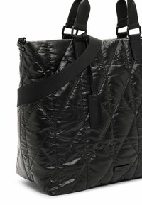 Sac cabas noir matelassé avec couture diagonale, double poignée, large bandoulière et petite étiquette de marque rectangulaire à l'avant.