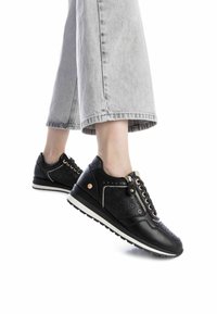 Zapatillas negras con diseño perforado, suela blanca y detalle de cremallera, combinadas con unos vaqueros cropped grises. Presentan acentos dorados y cierre con cordones.