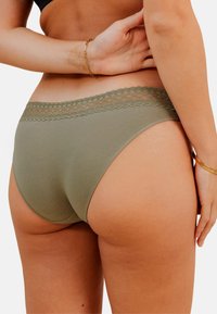 Culotte en coton vert olive avec une taille en dentelle à motif festonné. Texture lisse, design à jambe haute et détails de couture minimalistes.