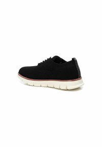 Zapatilla negra con parte superior de punto transpirable, patrón texturizado y suela blanca gruesa. Cuenta con un collar y una lengüeta acolchados para mayor soporte.