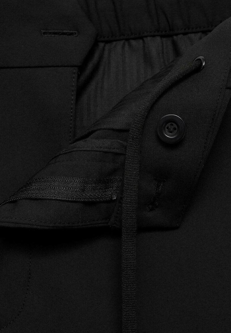 Ceinture élastique noire avec cordon de serrage, fermeture à bouton et texture de tissu lisse. Présente une poche intérieure au design plat.