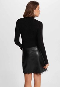 Zwarte geribbelde langetermijn top gecombineerd met een zwarte leren minirok met een kantafwerking. Gladde textuur met een aansluitend ontwerp.