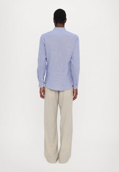 Camicia blu a maniche lunghe con motivo, orlo curvo, polsini con bottoni e colletto rialzato, abbinata a pantaloni beige chiaro a gamba larga.