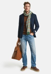 Marineblazer, brauner Pullover, karierter grüner Schal, blaue Jeans, braune Ledertasche, braune Schuhe mit dicken Sohlen, lockere Passform, strukturierte Materialien.