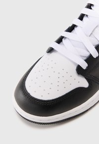 Sneaker bianco e nero con tomaia in pelle, punta perforata bianca e lacci bianchi piatti. Suola in gomma spessa con dettagli testurizzati.
