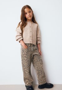 Bézs kötött kardigán gombos elől, párosítva leopárdmintás nadrággal és fekete fűzős cipővel. Simább textúra és laza szabás.