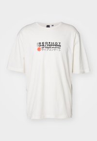 Hvid bomulds t-shirt med korte ærmer. Har teksten "RED HOT CHILI PEPPERS" i sort og rød, samt japanske tegn og stjerner som pynt.
