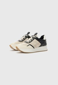 Sneakers featuring a beige canvas upper, black leather accents, and a stacked white sole with a textured gum rubber outsole.