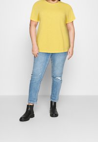Maglietta gialla a maniche corte con vestibilità ampia e colletto tondo. Abbinata a jeans strappati di un azzurro chiaro e stivaletti neri alla caviglia.